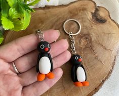 two small penguin keychains sitting on top of a piece of wood next to a plant