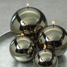 four shiny metal candles sitting on top of a silver plate