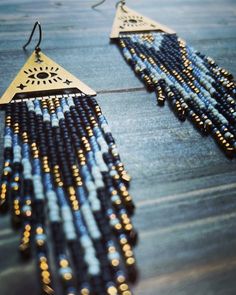 a pair of earrings with gold and blue beads hanging from it's sides on a wooden table