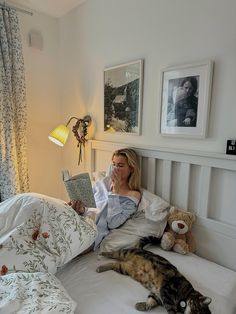 a woman laying in bed reading a book next to a cat