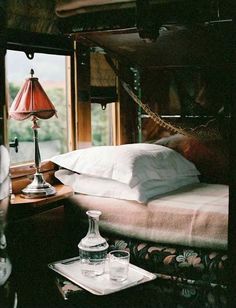 a bed sitting next to a window with a lamp on top of it and pillows