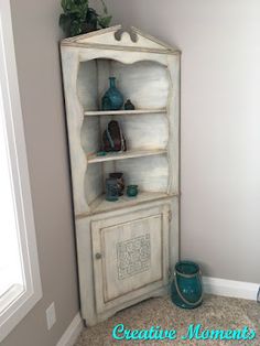 the corner of a room with a white bookcase and vases on top of it