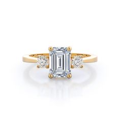 an emerald cut diamond ring with three diamonds on the band and side stones in rose gold