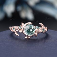 a close up view of a ring with an oval green stone and leaves on it