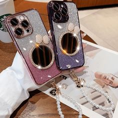 two phone cases with bows and pearls on them sitting next to each other, one is purple