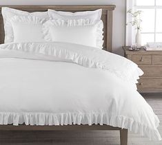 a bed with white ruffled sheets and pillows