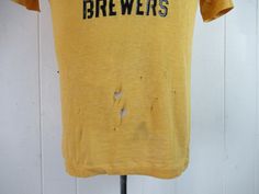 "Vintage 1960s yellow cotton t shirt with black graphics: Richmond Brewers Little League Baseball. Made by Southern Athletic. Size small. Actual measurements are: 38\" around the chest 38\" around the waist 17.5\" shoulder seam to shoulder seam 23\" overall length In \"wrecked\" condition with several holes." Vintage Fitted T-shirt With Letter Print, Fitted Yellow T-shirt With Screen Print, Vintage Yellow Tops With Screen Print, Vintage Yellow Top With Screen Print, Retro Mustard Cotton Top, Yellow Vintage Crew Neck Top, Fitted Vintage T-shirt With Screen Print, Vintage Yellow Short Sleeve T-shirt, Vintage Fitted Cotton T-shirt