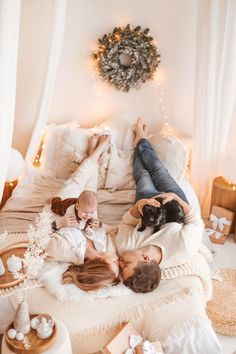 a woman laying on top of a bed next to a baby and an adult holding a cat