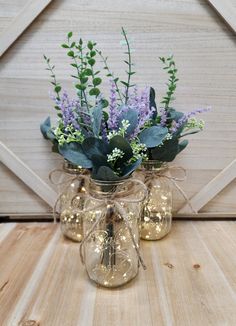 three glass vases with flowers and greenery in them