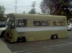 an old bus parked in a parking lot next to a curb with cars behind it