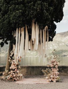 an outdoor ceremony setup with flowers and ribbons hanging from the tree, along with draping