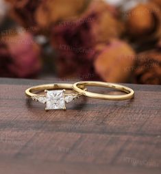 two gold wedding rings with a princess cut diamond in the middle on a wooden surface