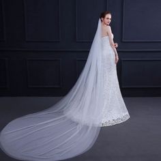 a woman in a wedding dress with a long veil on her head and shoulders, standing against a dark background