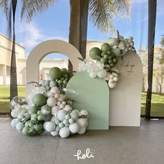 an arch decorated with balloons and greenery sits in front of a palm tree at the entrance to a building