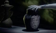 a hand reaching into a jar with writing on it and another vase in the background