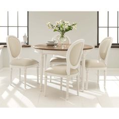 a dining room table with four chairs and a vase full of flowers on the table