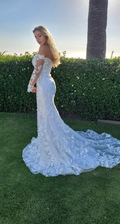 a woman in a white wedding dress standing on the grass with her arms behind her back