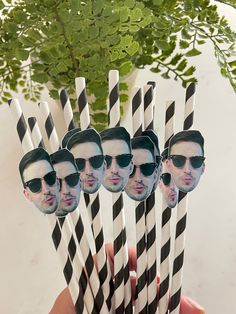 a hand holding six black and white striped drinking straws with photos of the same man on them