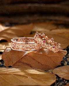 two wedding rings sitting on top of a leaf covered ground with leaves around them and the ring is surrounded by smaller pink stones