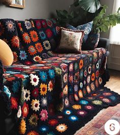 a couch covered in colorful crocheted blankets and pillows next to a potted plant