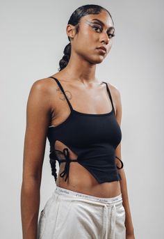 ArtcareShop's new take on a cut out top.  *Side cuts with strings to tie *Spagetti straps  *Petite fit (the model is wearing a size M). Size S Petite - chest 31.9in, length 16.5in Size M Petite - chest 33.4in, length 16.9 in Size L Petite - chest 34.9in, length 17.3in Size XL Petite - chest 36.4in, length 17.7in  Our favorite black  95% cotton and 5% polyester thick fabric (the same as our oversized t-shirts, biker shorts sets and Kai open back turtleneck). The model is wearing a size Petite M. ---------------------------------- ArtcareShop is a women-owned streetwear brand. From street to seam, we seamlessly blend edgy athleisure streetwear with luxurious designer quality to offer you a truly unique and effortless wardrobe that empowers you. Why Choose Us? * Crafted with Love: ArtcareShop Edgy Spring Tops With Built-in Bra, Edgy Camisole Tops For Summer, Edgy Summer Camisole Top, Trendy Crop Tank Top With Tie Straps, Trendy Crop Top Tank Top With Tie Straps, Black Cami Top With Tie Straps, Trendy Tie Straps Crop Top Tank, Trendy Strapped Crop Tops, Edgy Summer Tops With Straps