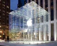 an apple store in the middle of a city at night with its glass facade lit up