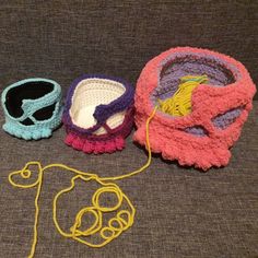 three crocheted hats sitting next to each other on a gray surface with a yellow string