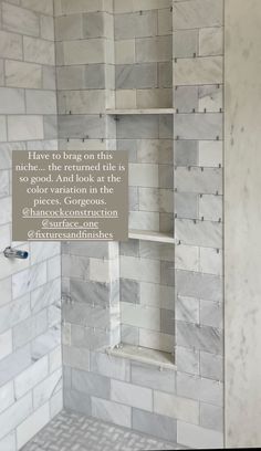 a bathroom with white and gray marble tile on the walls, shower head, and shelves