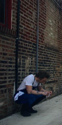 a man kneeling down next to a brick building