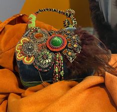 A piece of art on your arm! This Mary Frances bag has it all - velvet, beading, stone work, and feathers. You can carry it or display it, because it is just that beautiful! 7.5" wide x 8" tall x 3" deep Comes with dust bag. Mary Frances Black Green Orange Handbag, Bohemian Embellished Shoulder Bag For Gift, Bohemian Embellished Shoulder Bag As Gift, Mary Frances Bags, Mary Frances Handbags, Bowling Green Ky, Mary Frances, Bowling Green, Top Handle Bags