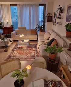 a living room filled with furniture next to a tall window covered in curtains and plants