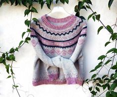 a knitted sweater hanging on a white wall with green leaves in the foreground