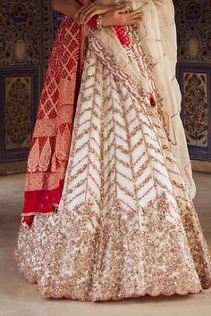 Ivory attached cancan lehenga with gold dabka, sequin, bead, red resham, french knots embroidery in chevron pattern. Paired with sweetheart neck padded blouse. Comes with cutwork border embroidered ivory dupatta and red bandhani woven dupatta. - Aza Fashions Traditional Gown With Cutdana For Ceremony, Traditional Ceremony Gown With Cutdana, White Ceremonial Gown With Traditional Drape, White Cutdana Wedding Dress, Ceremonial White Gown With Traditional Drape, White Anarkali Gown For Ceremonial Occasions, White Dress With Zari Work For Ceremony, White Gown With Resham Embroidery For Ceremony, Bollywood Style White Ceremony Dress