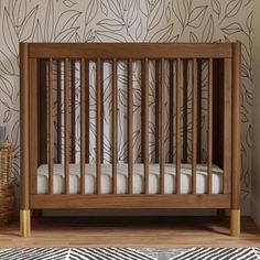 a baby crib in front of a wall with leaves on it and a basket next to it