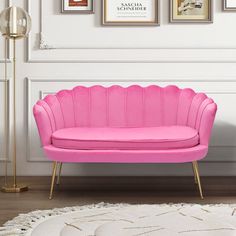 a pink couch sitting on top of a white rug next to a lamp and pictures