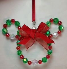 a christmas ornament hanging from a red ribbon on a white table with green and red beads