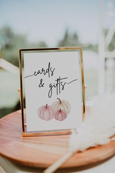 a card and gifts sign sitting on top of a wooden table next to a feather