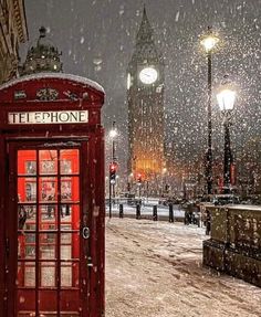 a red phone booth sitting in the middle of a snow covered street next to a clock tower