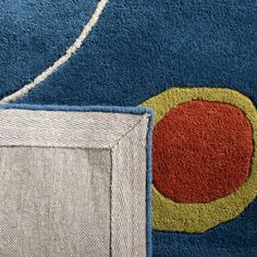 a blue rug with an orange and yellow circle on the center is next to a white square