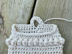 a white crocheted bag hanging from a wooden fence next to a piece of wood