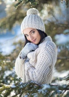 a woman wearing a white sweater and hat in the snow with her hands on her chest