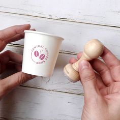 two hands holding coffee cups with wooden stoppers in front of white painted wood planks