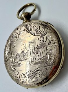 This early and rare Victorian locket dates from the 1850s to 1860s.  It features FOUR places for photos with FOUR pieces of original beveled glass and FOUR photos from the period!  I believe the photos are ambrotypes.  It has front and back covers with detailed and decoratively engraved designs--a village scene on one side surrounded by large plumes and large feathery plumes on the other side with a small banner near the bottom, possibly for tiny personalization.  To access the compartments, jus Victorian Engraved Round Pocket Watch, Victorian Medallion Pocket Watch For Formal Occasions, Antique Locket Pocket Watch For Formal Occasions, Engraved Antique Gold Pocket Watch For Formal Occasions, Timeless Engraved Compact Pocket Watch, Victorian Gold Engraved Pocket Watch, Victorian Round Pocket Watch Collectible, Antique Bronze Pocket Watch With Locket, Antique Medallion Pocket Watch For Wedding