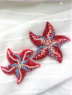 two red, white and blue beaded starfish brooches on a white cloth