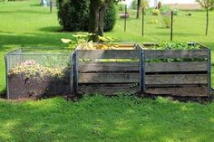 a wooden box filled with lots of dirt and plants next to a fenced in area