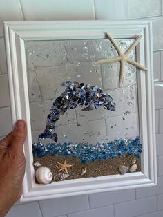 a hand holding up a framed photo with shells and starfish