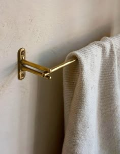 a towel hanging on the side of a white wall next to a metal hook with gold handles