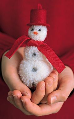 a person holding a small white snowman in their hands with a red scarf around it's neck