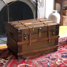 an old trunk sitting on top of a rug in front of a fire place and fireplace