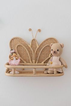 a teddy bear sitting on a bench with a butterfly shaped wall hanging above it's head